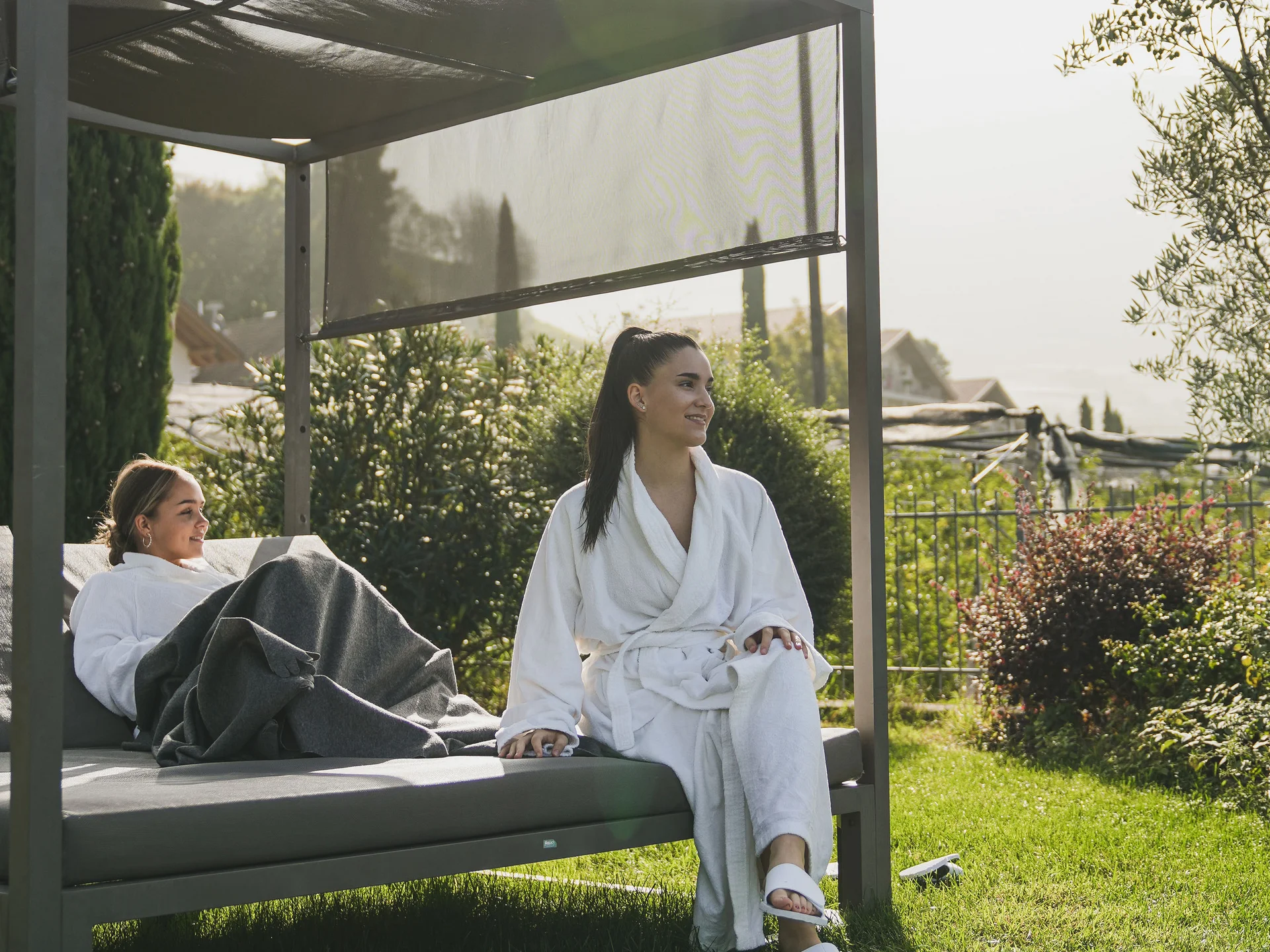 Zwei Frauen in Bademänteln entspannen im Garten auf einem überdachten Tagesbett