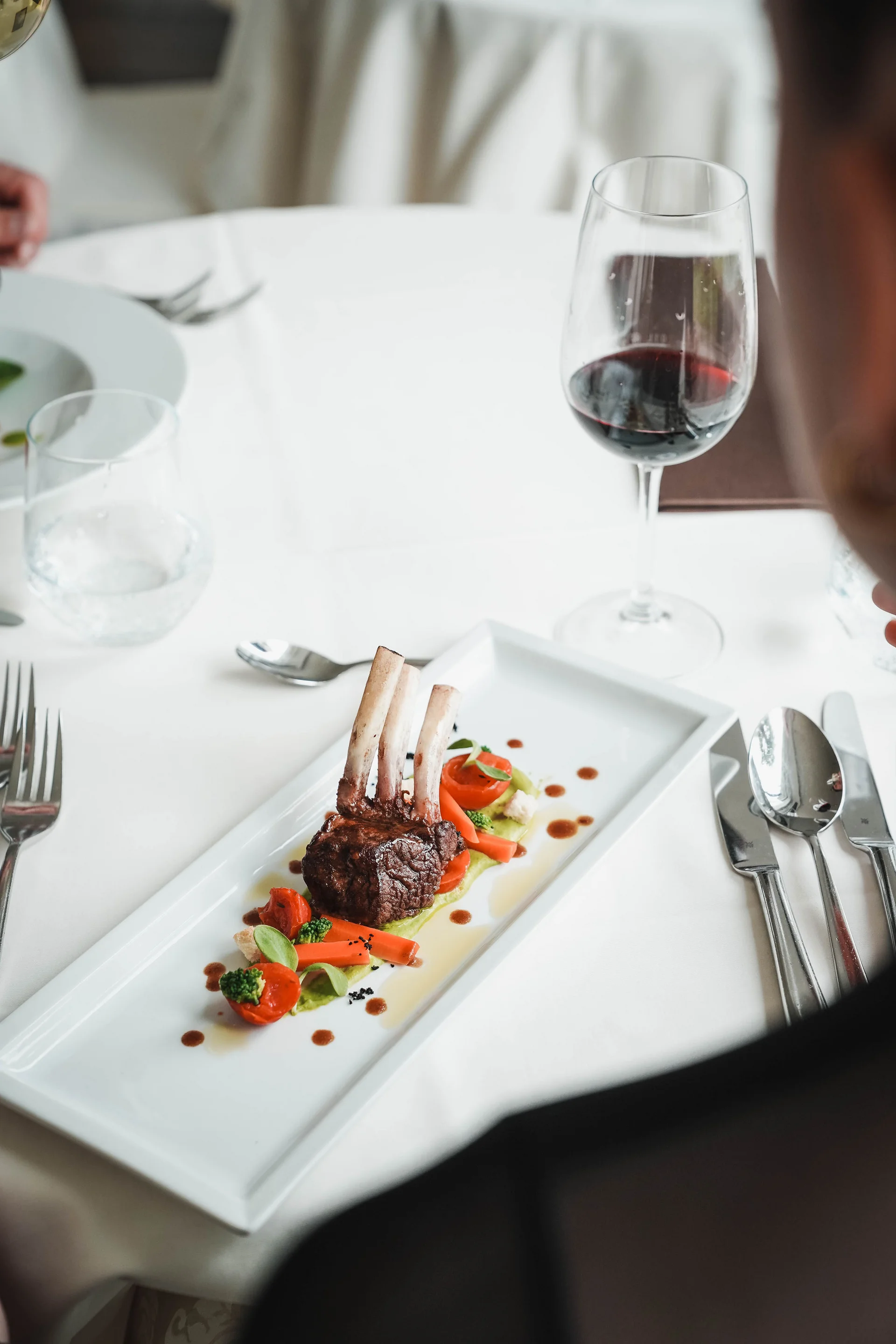 Echt regional: das Essen in eurem Genusshotel bei Meran Fein angerichtetes Lammkarree mit Gemüse und Rotwein am Tisch