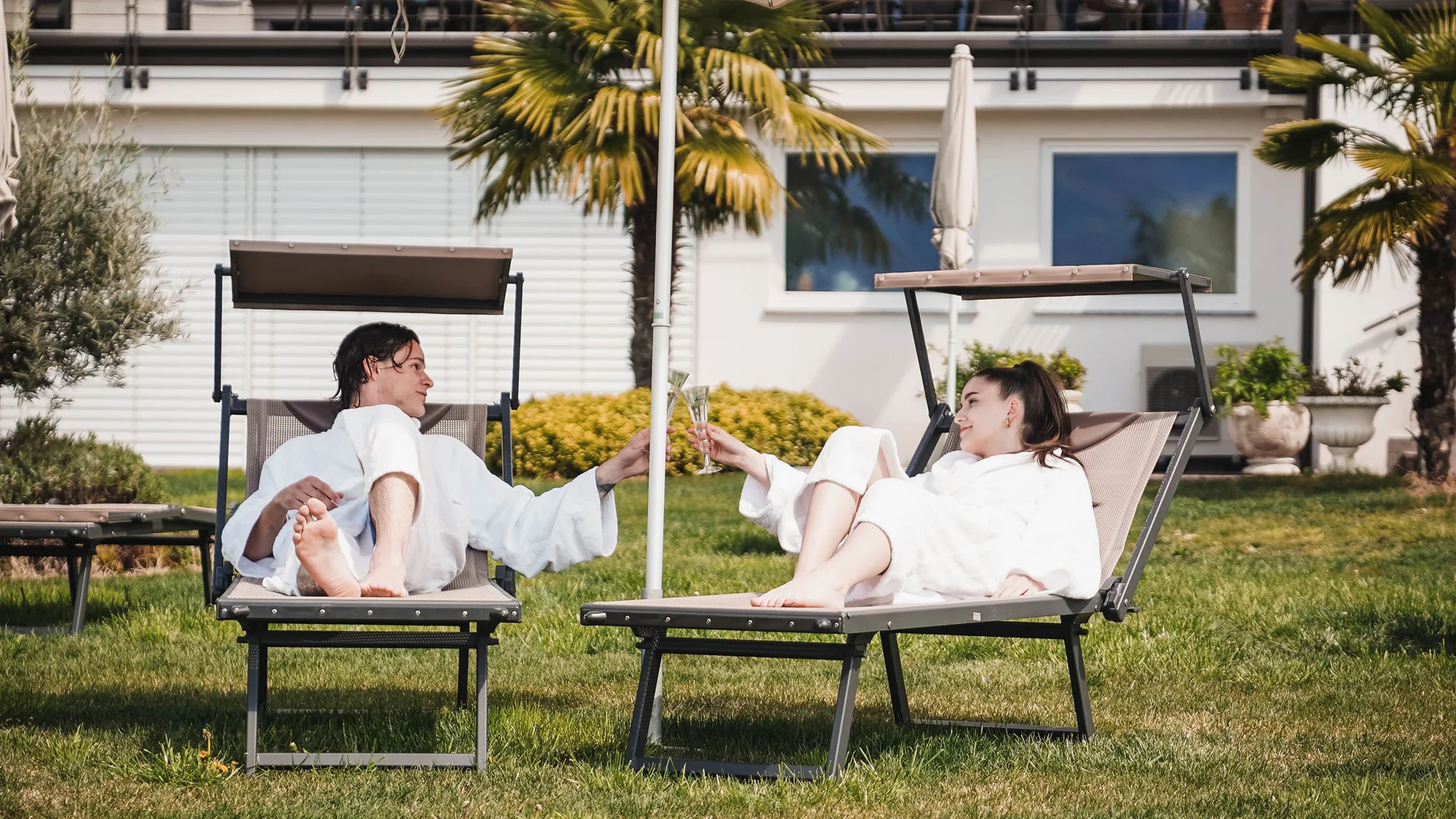 Impressionen in #echtzeit Paar in Bademänteln stößt bei Pool auf Liegestühlen an