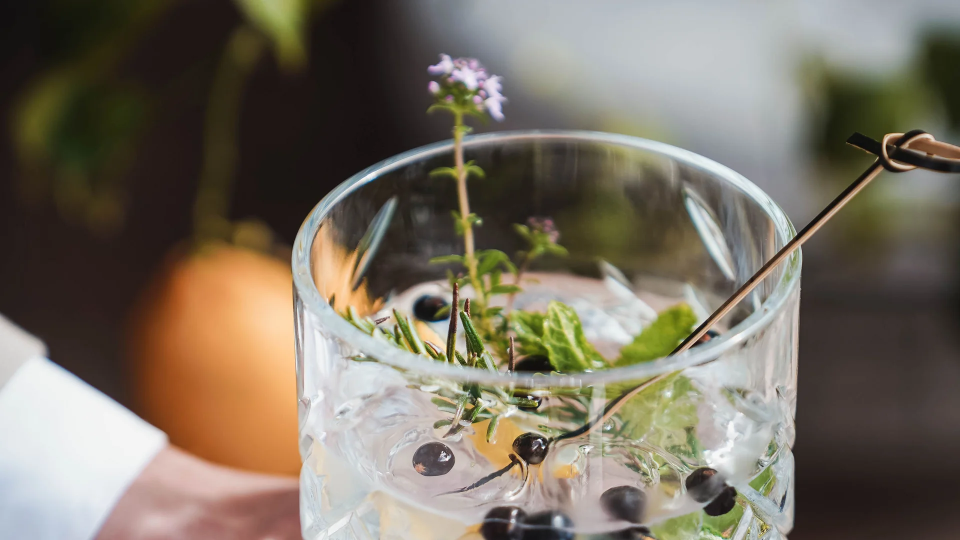 Impressionen in #echtzeit Hand hält ein Kristallglas mit einem klaren Cocktail und Kräutergarnitur