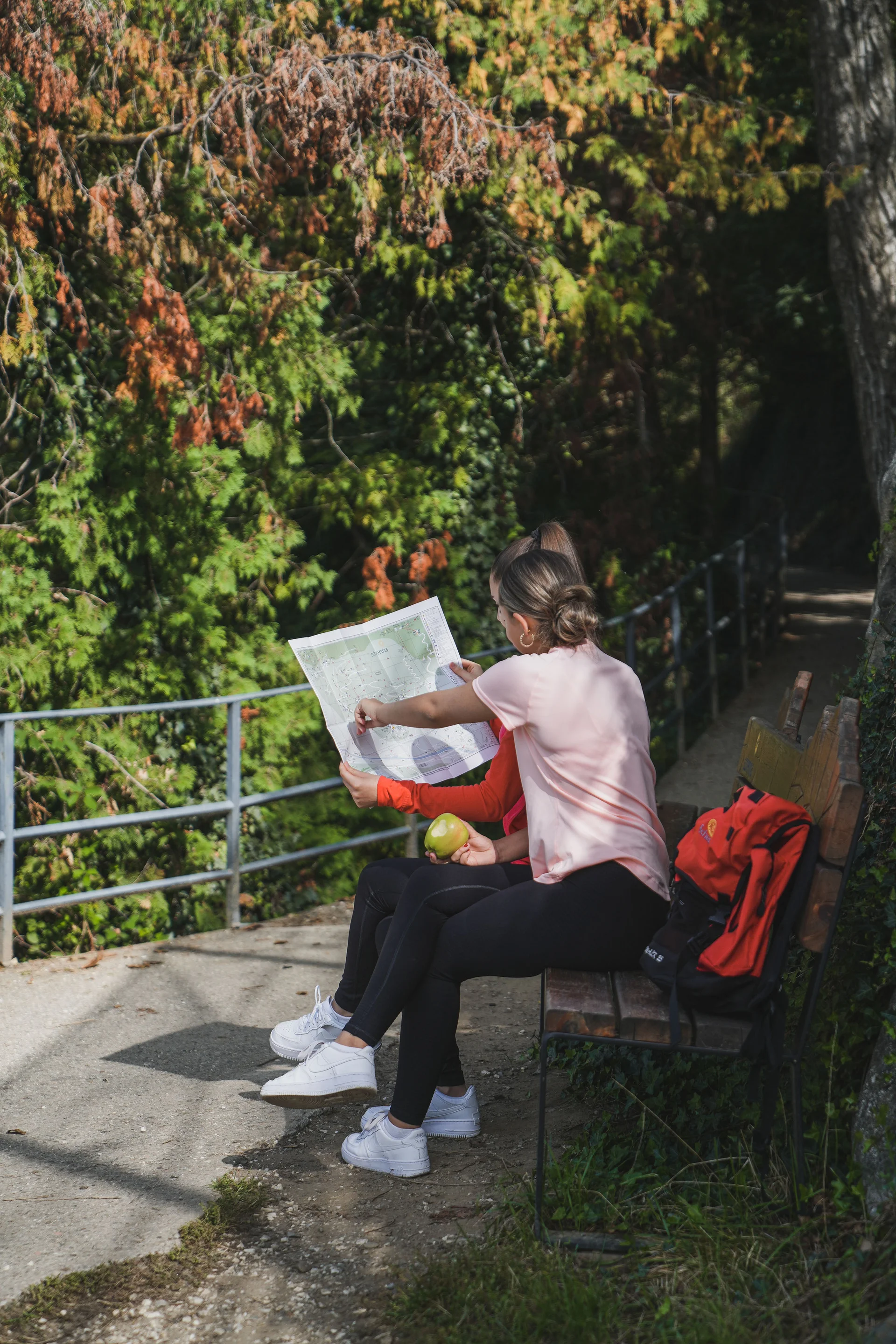 Zwei Frauen sitzen auf einer Bank und betrachten eine Karte im Wald