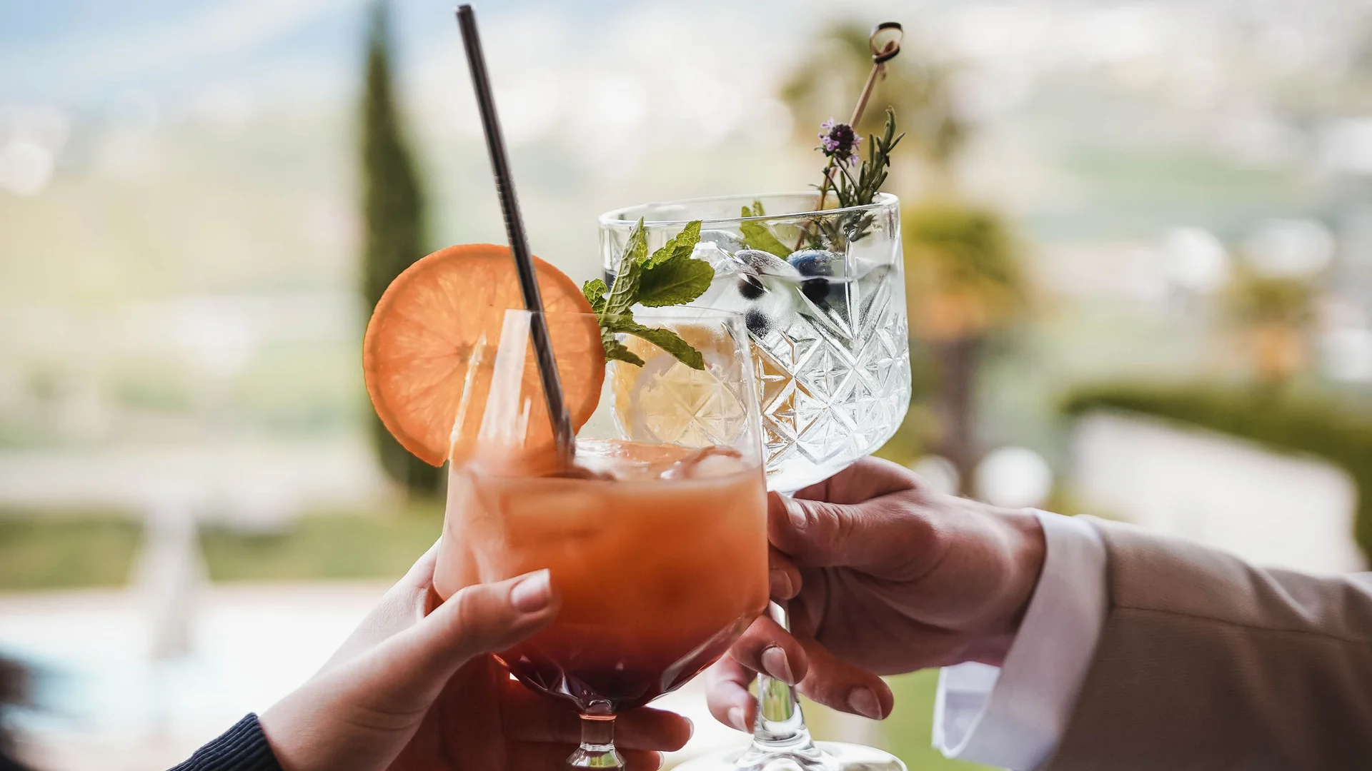 Impressionen in #echtzeit Zwei Hände stoßen mit Cocktails mit Reifen und Kräutern am Balkon an
